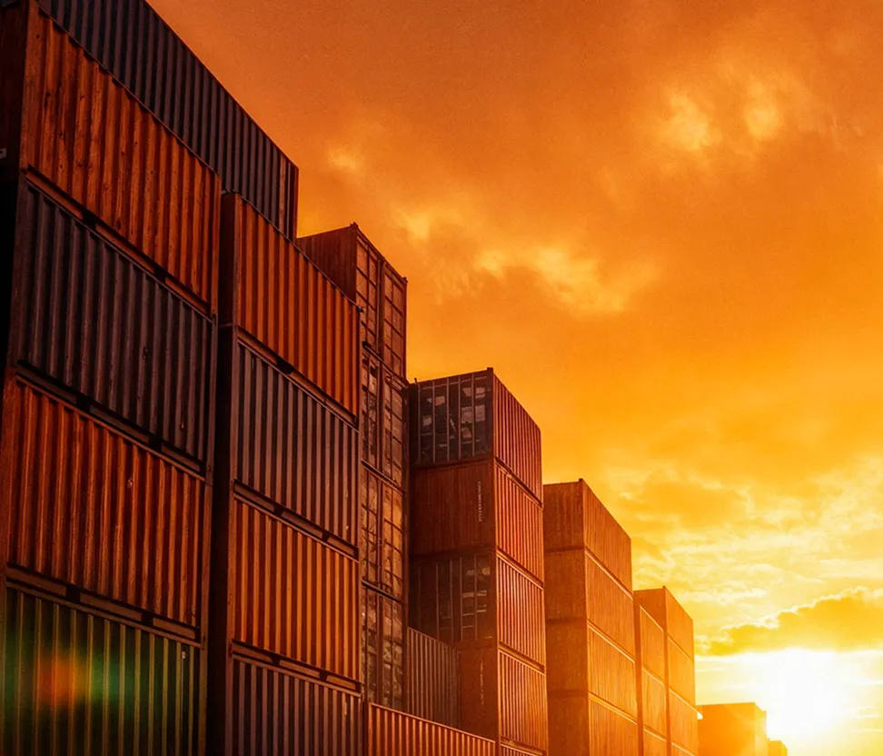 Stacked shipping containers at sunset under an orange sky with clouds.